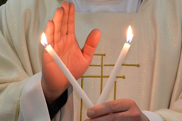 Priester hält Kerzen zum Blasiussegen